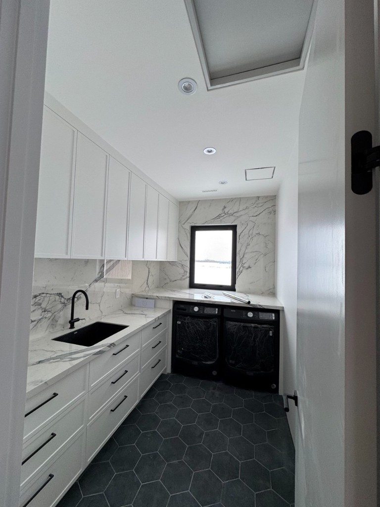 Laundry room with white cabinets, marble-look surfaces, black fixtures, and hex floor tile.