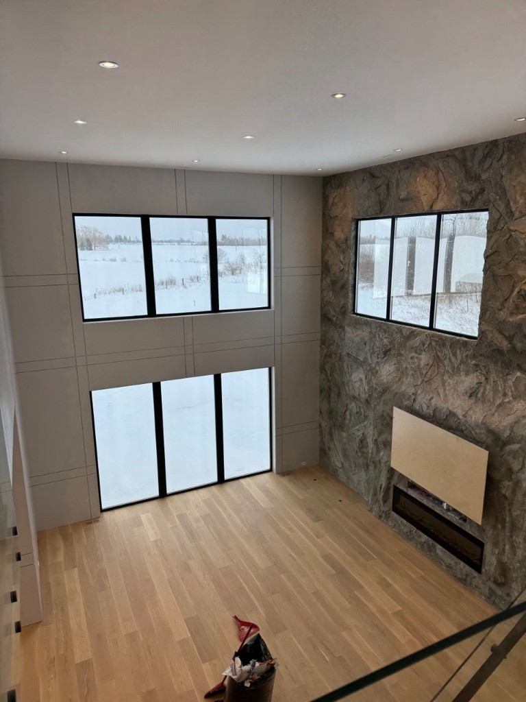 Open living space with high ceiling, grey paneled walls, stone feature wall, and hardwood floors.